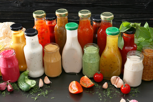 Bottles with different tasty sauces and vegetables on dark table