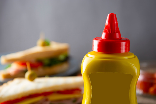 Yellow mustard squeeze bottle container with no label. Breakfast sandwich on background, Food product